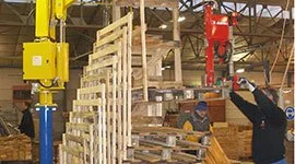 Dalmec manipulators handling stacked wooden pallets in a warehouse as workers position the load.