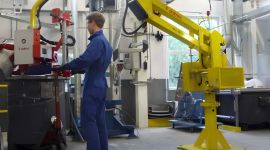 Operator using a column-mounted industrial manipulator with a custom gripper to safely lift and position a heavy industrial component in a manufacturing facility.
