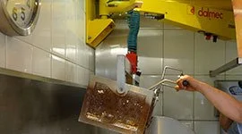 Dalmec manipulator with gripping tool handling a container over a wash station as a worker assists nearby.