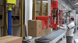Industrial vacuum box lifting manipulator lifting a cardboard carton on a conveyor for safe and ergonomic material handling.
