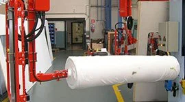Dalmec manipulator with dual gripping arms lifting a large fabric roll in a textile facility.