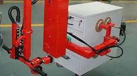 Dalmec manipulator with dual gripping arms handling a furniture cabinet unit in a manufacturing facility.