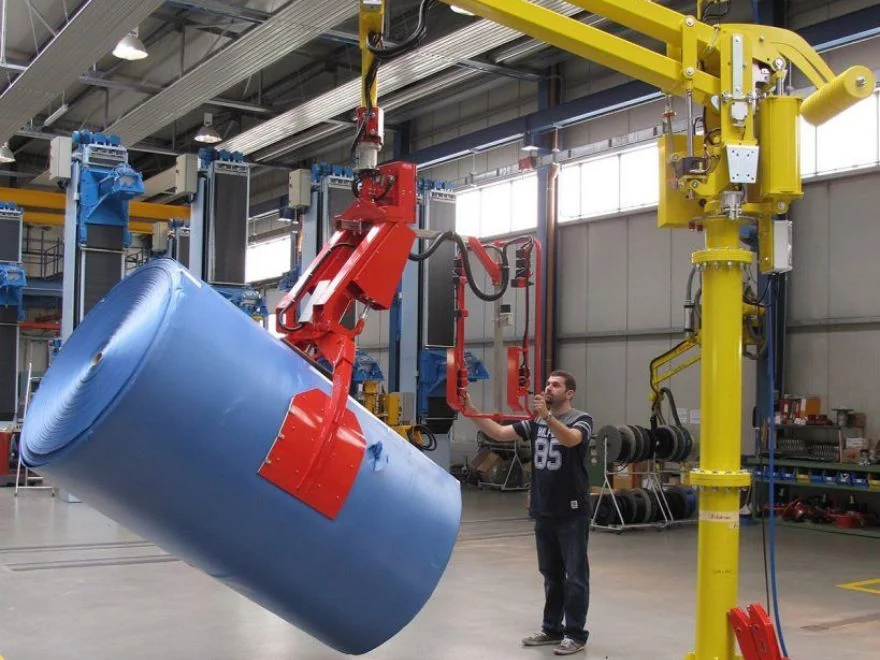 Dalmec manipulator with clamp gripping tool tilting a large blue insulating material reel as a worker guides positioning.