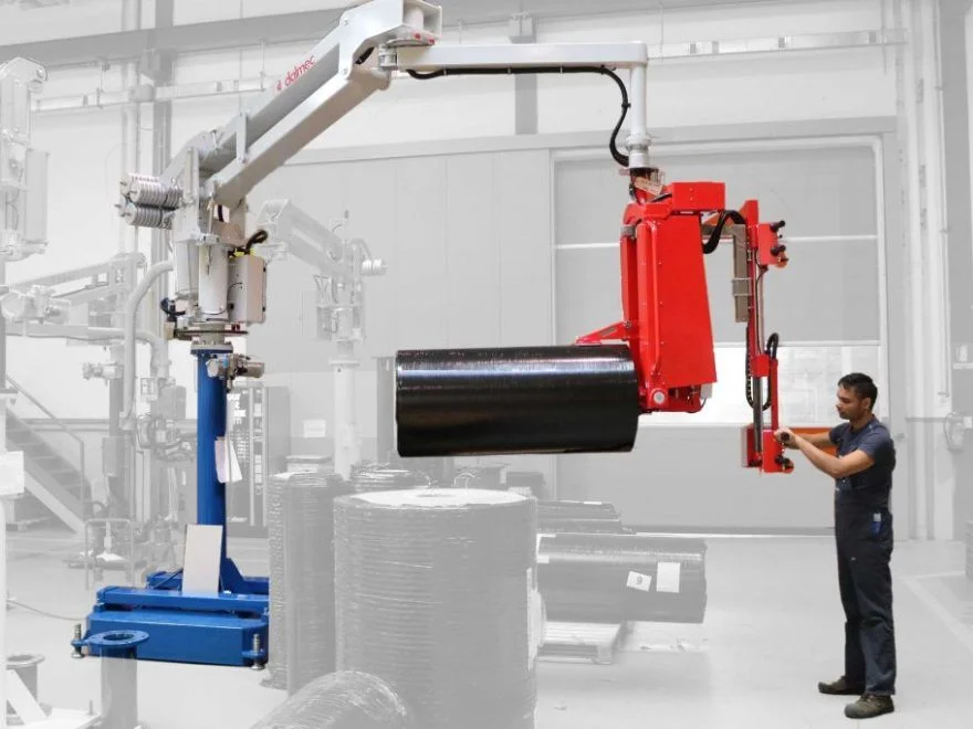 Dalmec manipulator with gripping tool lifting a black insulation material reel as a worker guides the load.