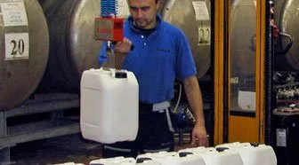 Worker using a Dalmec manipulator with hook attachment to lift and move plastic jerrycans in a warehouse