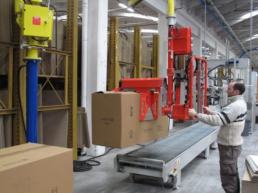Dalmec manipulator with mechanical gripper transferring a large cardboard package from a roller conveyor in a manufacturing warehouse