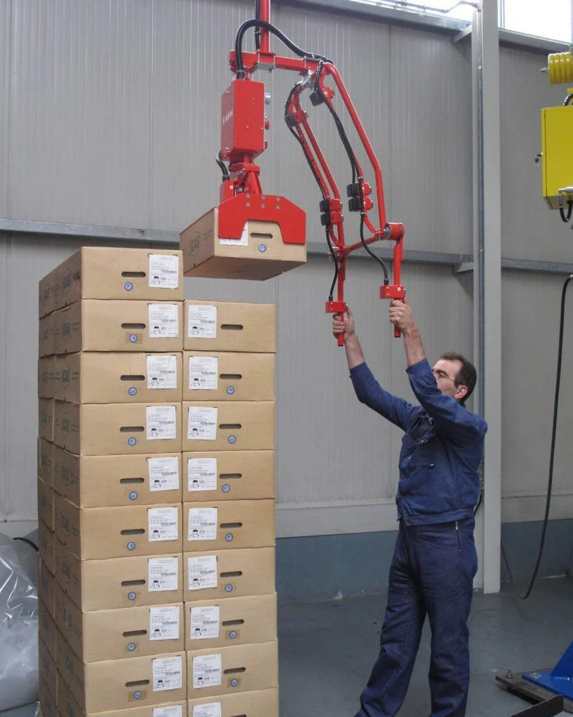manipulator with custom gripping tool lifting a cardboard carton box from a high pallet stack, operated effortlessly by a single worker in a warehouse