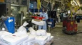 Dalmec manipulator handling chemical powder bags in a chemical processing facility, with workers in full PPE managing materials safely