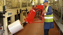 Dalmec manipulator with custom gripper handling a large plastic film reel in a chemical and packaging production facility