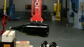 Dalmec manipulator with custom gripping tool handling large dark glass bottles in a food and beverage production facility