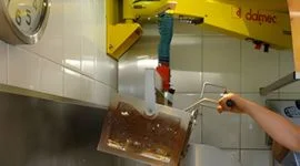 Dalmec manipulator with custom gripping tool handling a food container in a commercial kitchen or food processing environment