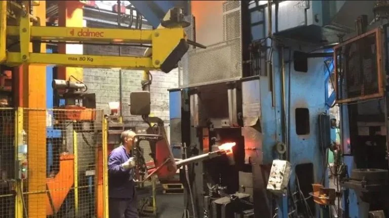 Dalmec manipulator, rated to 80 kg capacity, handling a hot casting piece near a furnace as a worker in protective gear operates it.