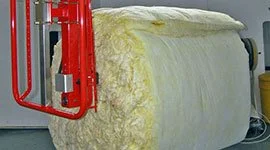 Dalmec manipulator with custom gripper handling a large fibreglass insulation roll in a building materials facility