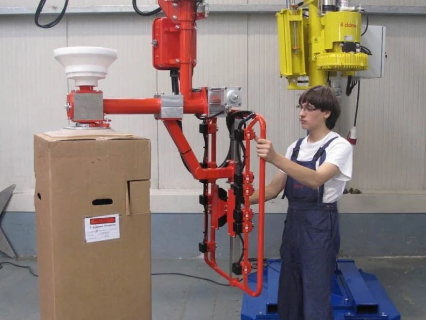 Dalmec manipulator with vacuum suction cup tool positioning a large cardboard box in an industrial facility, operated by a single worker