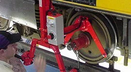 Dalmec manipulator with custom gripping tool handling a heavy rail wheel and bogie assembly during train maintenance