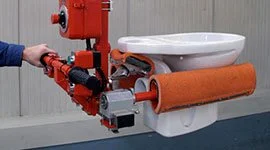 Dalmec manipulator with custom gripping tool handling a ceramic toilet and sanitary ware in a building products manufacturing facility