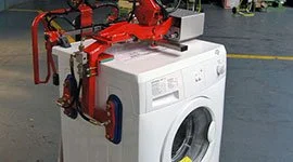 Dalmec manipulator with custom top-mounted gripping tool handling a front-load washing machine during electromechanical assembly