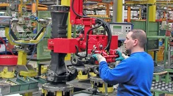 Worker using a Dalmec manipulator to position a mechanical component on an assembly line in a manufacturing plant