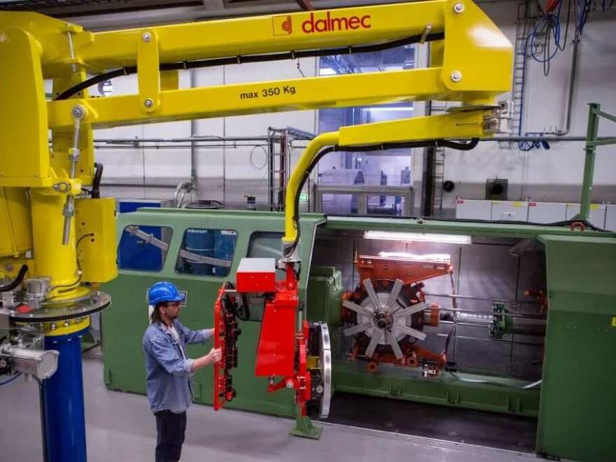 Dalmec manipulator, rated to 350 kg capacity, positioning a roll of metallic banding at a coil-winding machine as a worker guides the load.