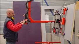 Dalmec manipulator with clamp gripping tool lifting a decorative panel as a worker guides positioning.