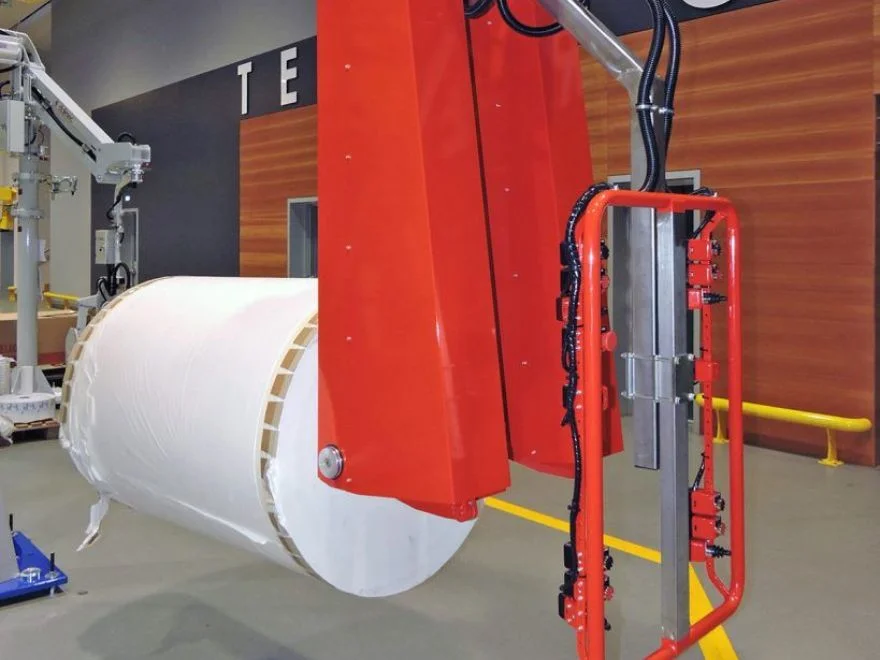 Dalmec manipulator with clamp-style gripping tool handling a large paper reel in a manufacturing facility.
