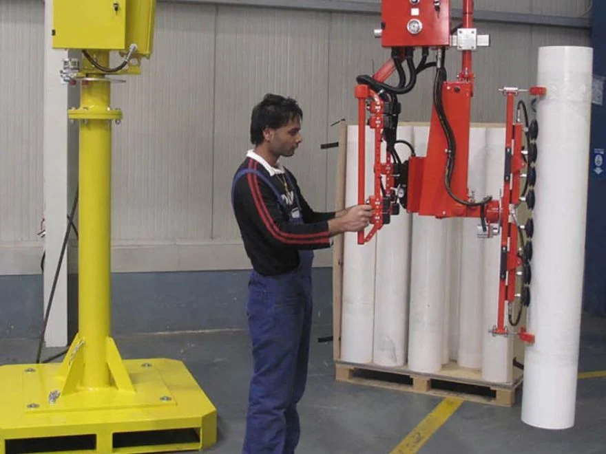 Dalmec manipulator with multi-clamp gripping tool lifting plastic film reels from a pallet as a worker guides the load.