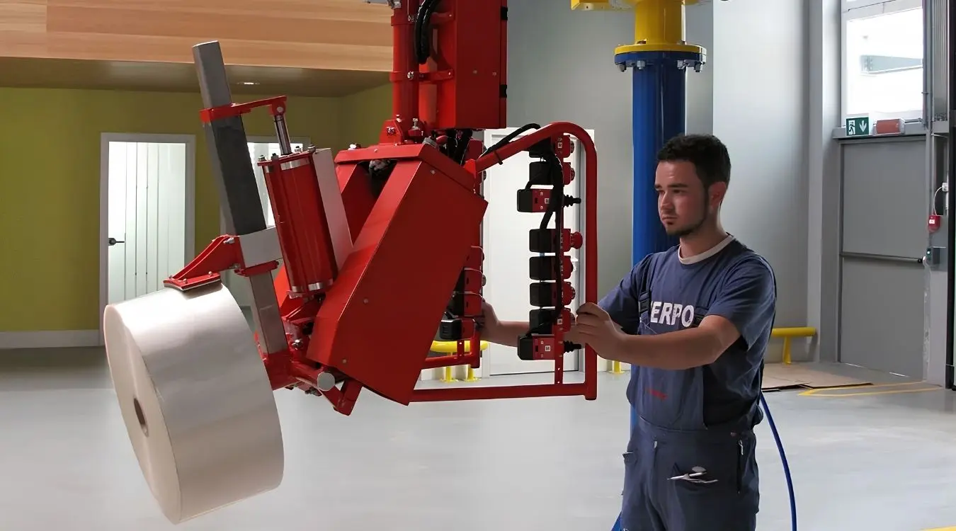 Dalmec pneumatic industrial manipulator with reel gripping tooling lifting and tilting a large plastic film reel, operated by a single worker