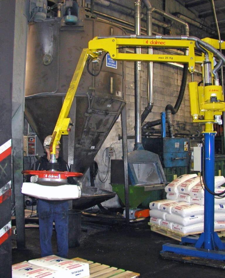 Dalmec manipulator, rated to 25 kg, lifting a sealed bag of resin material for tipping into a hopper as a worker guides positioning.