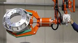 Dalmec manipulator with circular gripping tool handling a metal rim casting in a foundry facility.