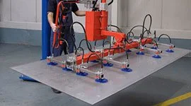 Worker operating a Dalmec manipulator with vacuum suction cups to lift and position a large metal sheet