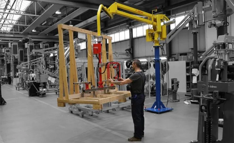Dalmec manipulator with clamp gripping tool positioning a timber frame component on a production jig as a worker guides placement.