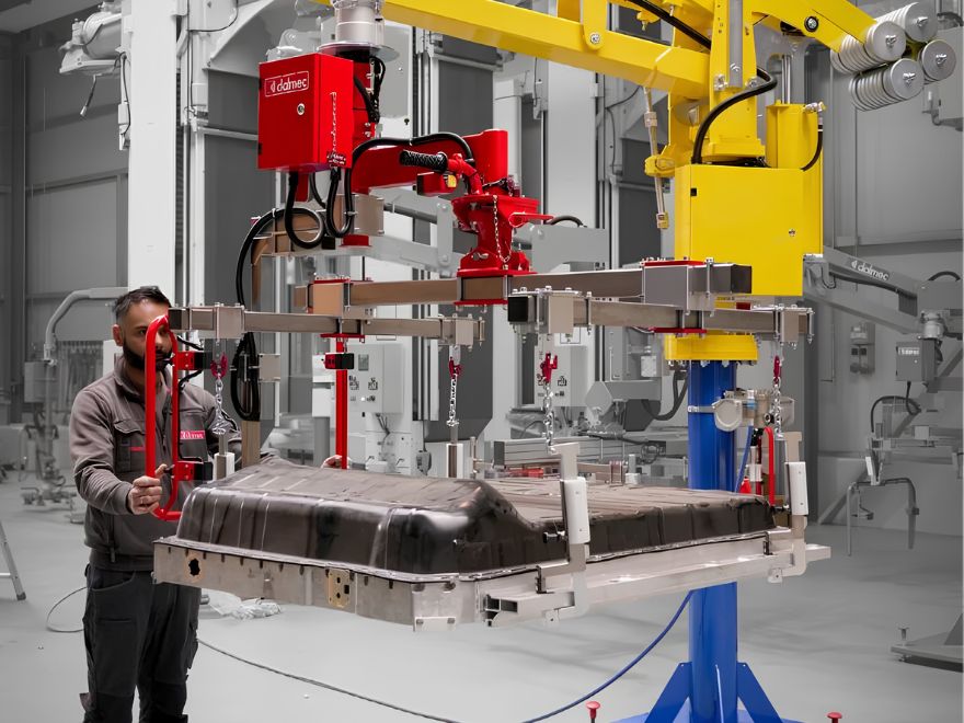 Operator using a column-mounted industrial manipulator with a custom gripper to lift and position a large molded automotive component in a manufacturing facility.