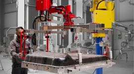 Operator using a column-mounted industrial manipulator with a custom gripper to lift and position a large molded automotive component in a manufacturing facility. SEO-friendly file name: