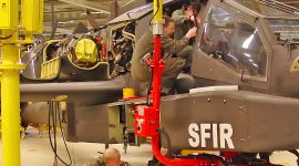 Column-mounted industrial manipulator with a custom support fixture assisting technicians during helicopter cockpit assembly and maintenance in an aerospace manufacturing facility.