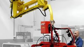Operator using an overhead industrial vacuum manipulator with a multi-suction cup gripper to lift and position a large flat panel or sheet in a manufacturing facility.