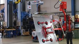 Industrial vacuum metal sheet lifting manipulator with suction cups handling a large sheet metal panel for safe, precise, and ergonomic material handling in a manufacturing facility
