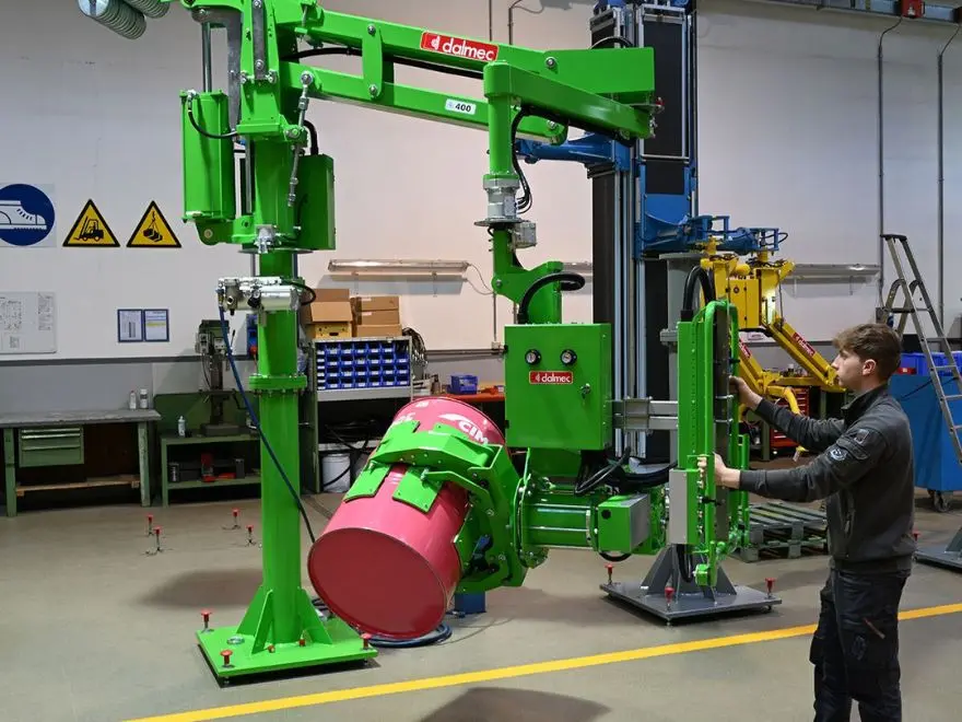 Dalmec pneumatic industrial manipulator with drum gripper performing a controlled tip of a 205-litre steel drum, operator guiding the load