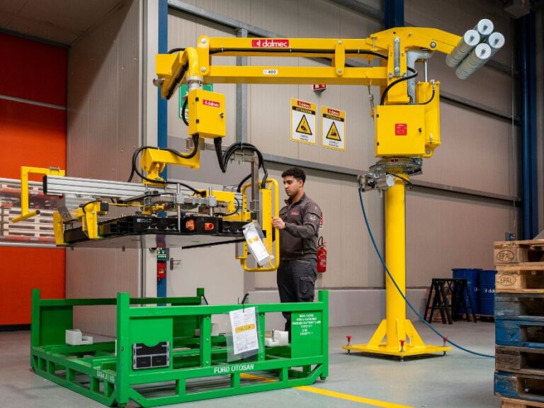 Dalmec pneumatic industrial manipulator with jaw gripper handling a high-voltage EV battery on a vehicle assembly line, operator guiding the load one-handed