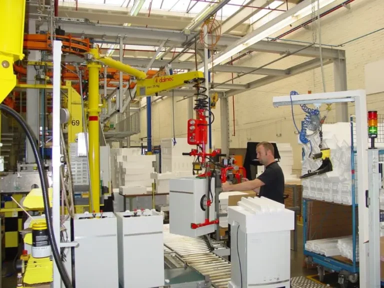 Dalmec pneumatic manipulator with vacuum tooling lifting a finished appliance unit at an end-of-line packing station, operator guiding the load one-handed