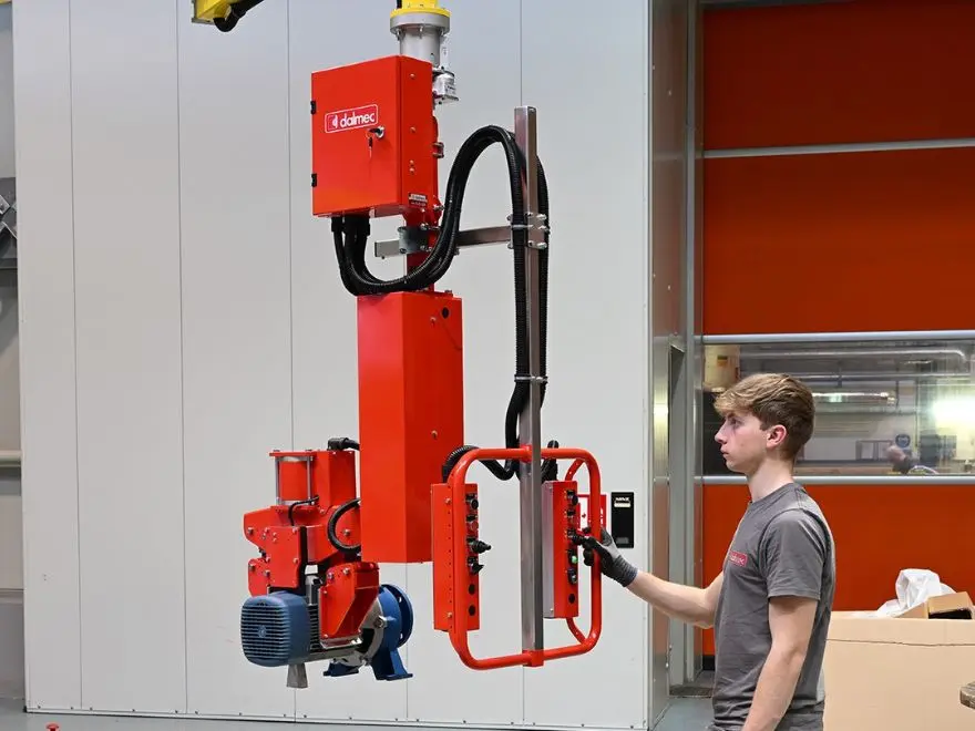 Dalmec pneumatic industrial manipulator lifting an electric motor on an assembly line, operator guiding the load one-handed